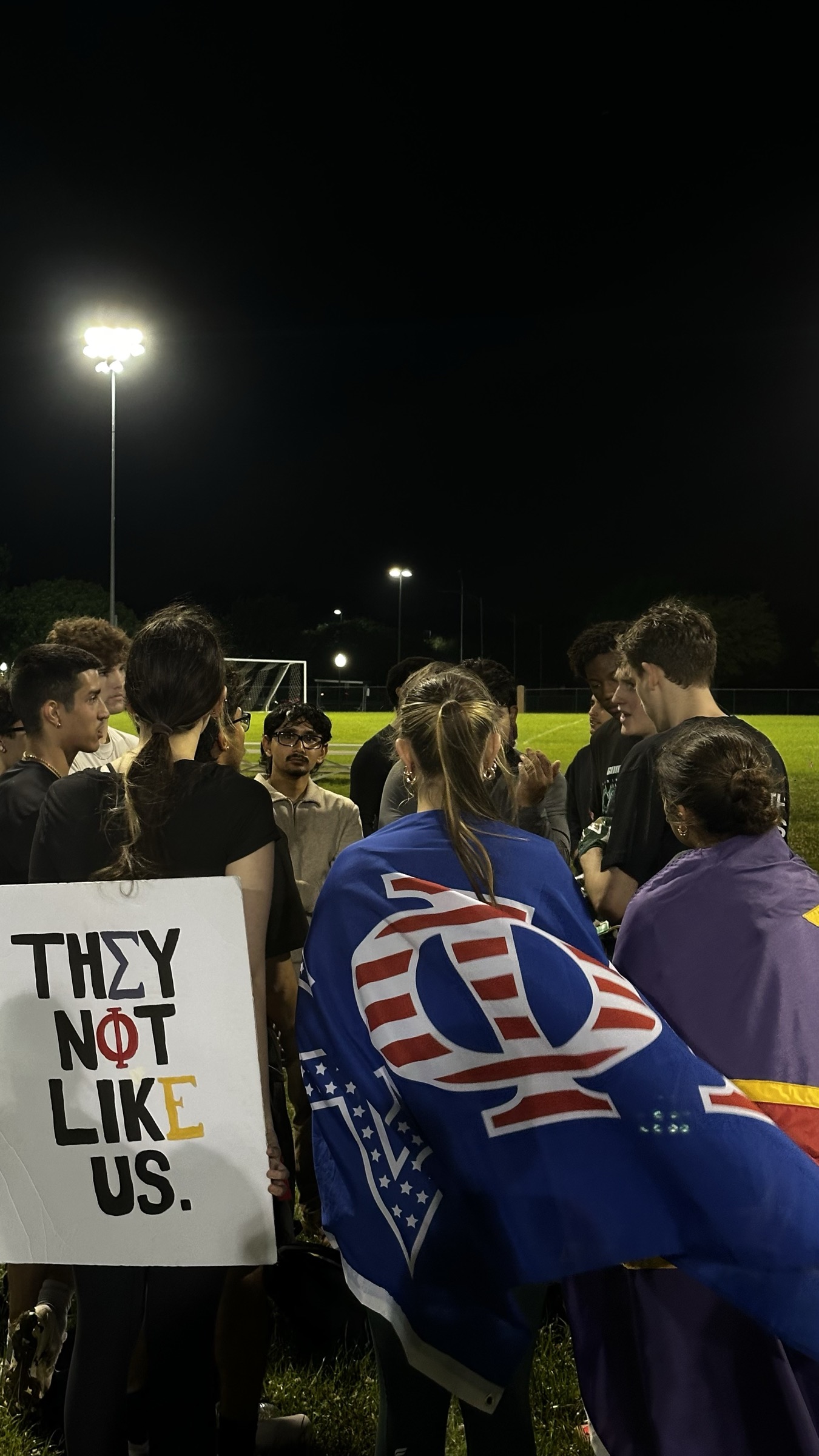Brothers gathered on the intramural field holding a 'They not like us' sign.